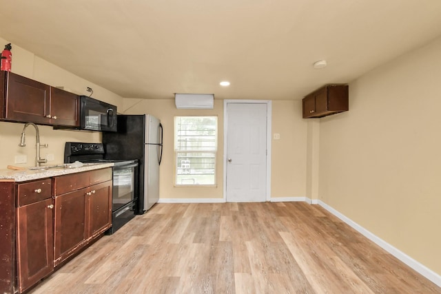 kitchen featuring baseboards, light wood-type flooring, light stone counters, a sink, and black appliances