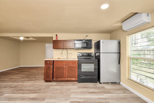 kitchen featuring baseboards, a wall mounted air conditioner, a sink, light wood-style flooring, and black appliances