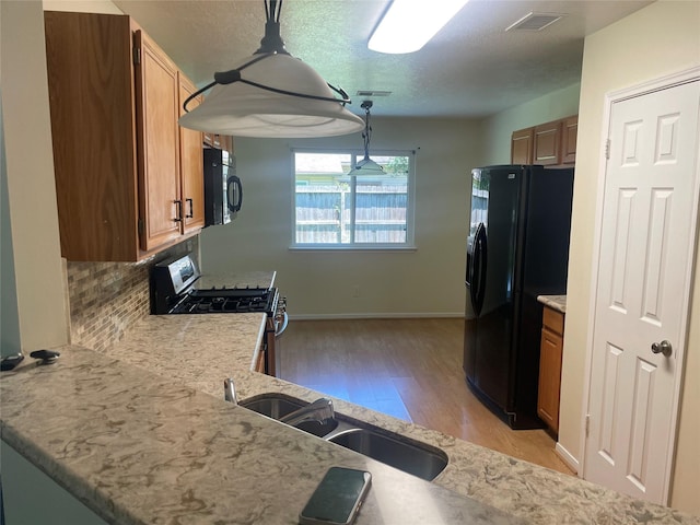 20018 Big Timber Dr, Humble, TX 77346 - kitchen with black appliances, a sink, light wood-style flooring, tasteful backsplash, and brown cabinets
