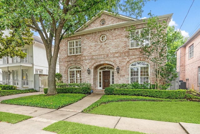view of front of home featuring brick siding, a front yard, and central AC