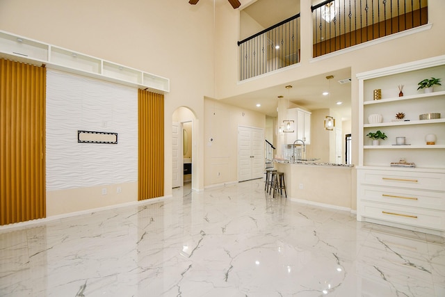 6326 Prince Place Dr, Rosenberg, TX 77471 - living room featuring arched walkways, light marble finish floors, ceiling fan, baseboards, and a high ceiling