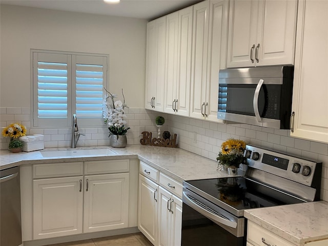 kitchen featuring light stone counters, a sink, stainless steel appliances, white cabinetry, and tasteful backsplash