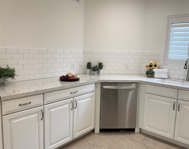 kitchen with stainless steel dishwasher, decorative backsplash, white cabinets, a sink, and light tile patterned floors