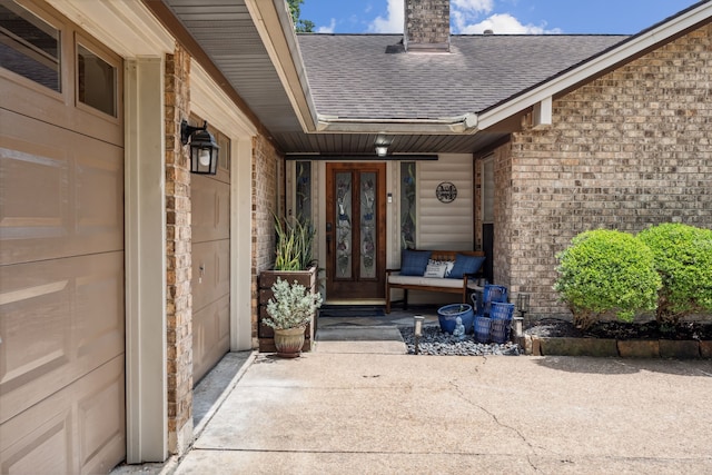 property entrance with french doors, a shingled roof, brick siding, a chimney, and covered porch