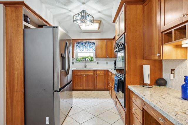 kitchen with stainless steel refrigerator with ice dispenser, brown cabinetry, a sink, decorative backsplash, and light tile patterned floors