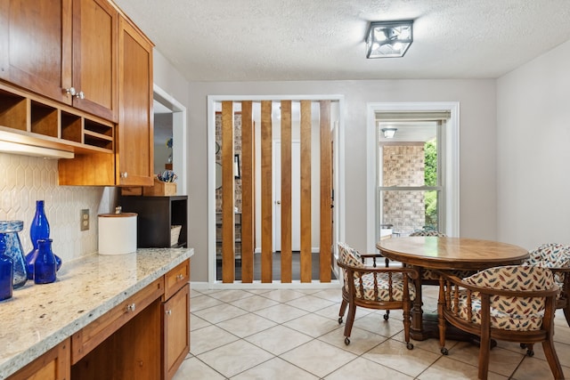 kitchen featuring open shelves, light tile patterned floors, a textured ceiling, brown cabinetry, and light stone countertops