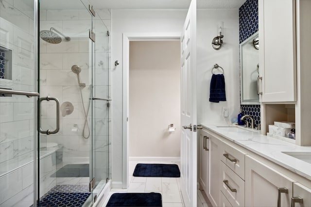 full bath with a stall shower, marble look tiles, baseboards, and double vanity