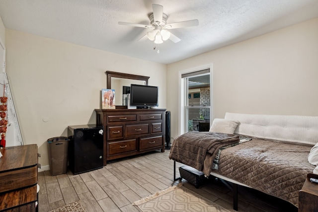 bedroom with light wood-type flooring, refrigerator, a ceiling fan, and a textured ceiling