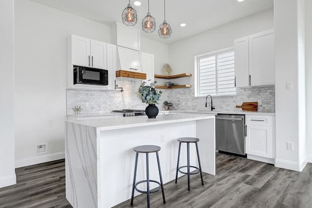 kitchen featuring dishwasher, black microwave, a kitchen island, decorative backsplash, and a sink