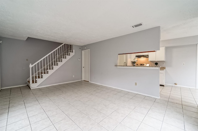 unfurnished living room with a textured ceiling, visible vents, baseboards, stairs, and light tile patterned flooring