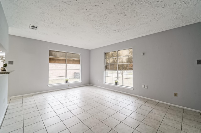 tiled empty room with visible vents, a textured ceiling, and baseboards