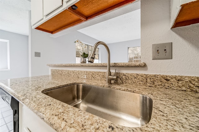 interior details featuring white cabinetry, light stone countertops, a sink, and dishwashing machine