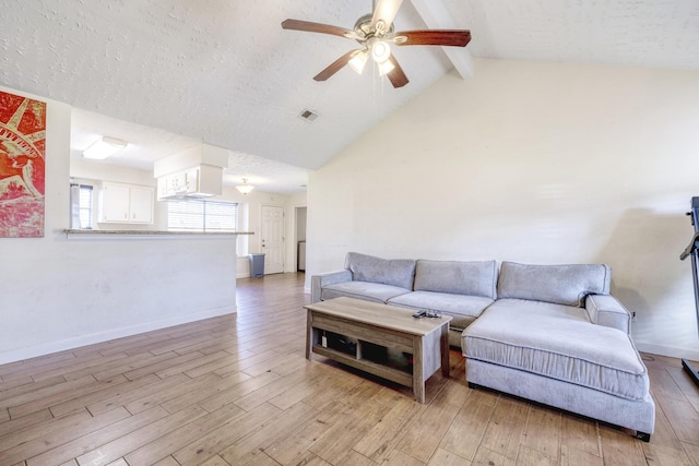 living room with ceiling fan, visible vents, baseboards, light wood-style floors, and vaulted ceiling with beams