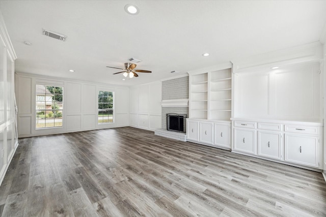 unfurnished living room featuring ornamental molding, a decorative wall, ceiling fan, and visible vents
