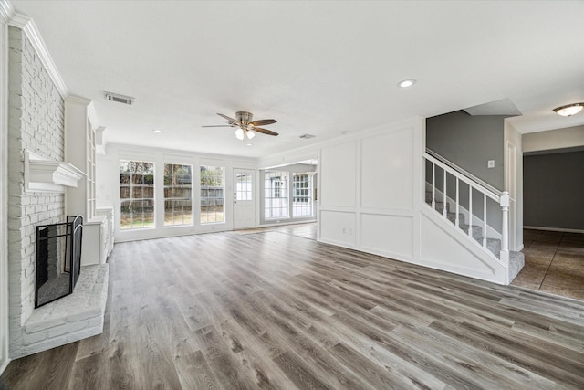 unfurnished living room featuring ceiling fan, a fireplace, wood finished floors, visible vents, and stairway