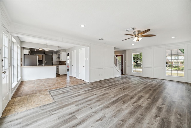 unfurnished living room with recessed lighting, a ceiling fan, a decorative wall, and stairs