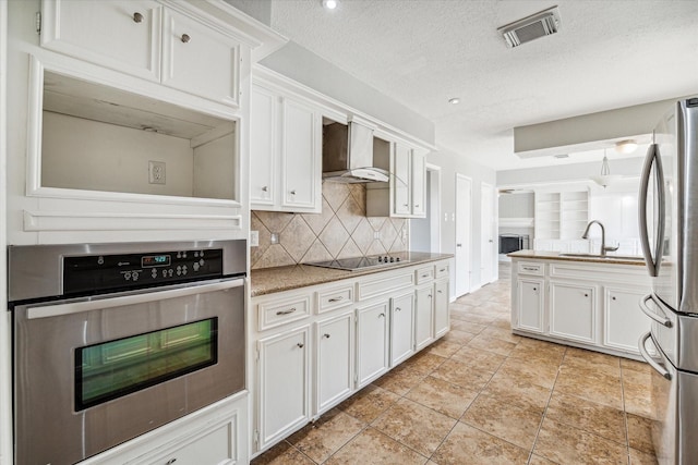 kitchen featuring white cabinets, appliances with stainless steel finishes, a sink, wall chimney exhaust hood, and visible vents