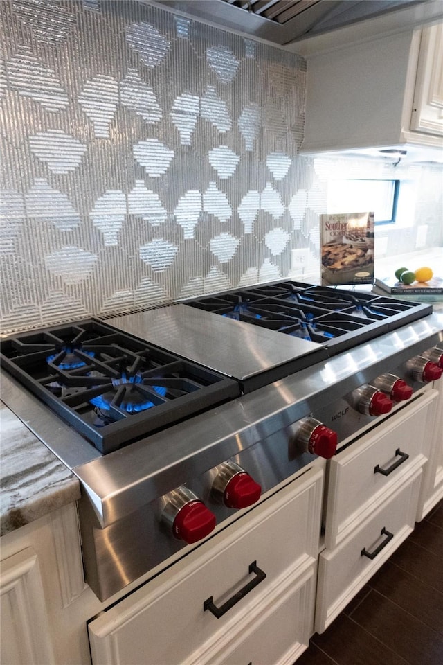 kitchen view of decorative backsplash, stainless steel gas stovetop, white cabinetry, and light countertops