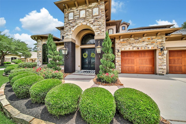property entrance featuring stone siding, french doors, concrete driveway, and an attached garage
