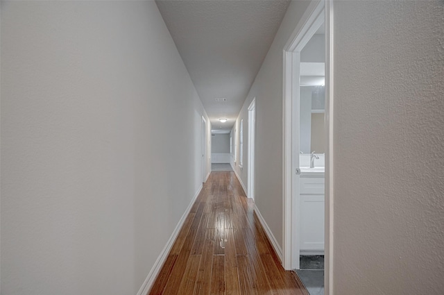 corridor with a sink, baseboards, and hardwood / wood-style flooring