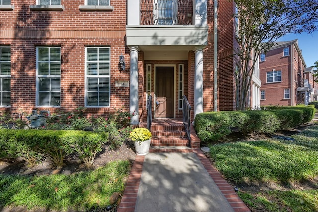 view of exterior entry with a balcony and brick siding