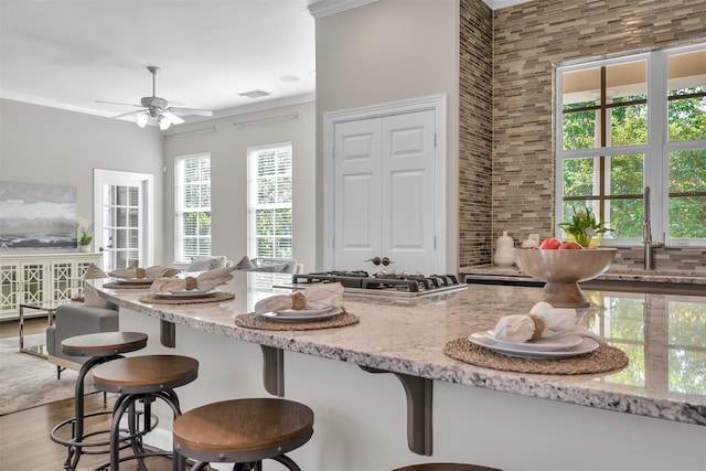 kitchen featuring visible vents, wood finished floors, a breakfast bar, light stone counters, and a ceiling fan