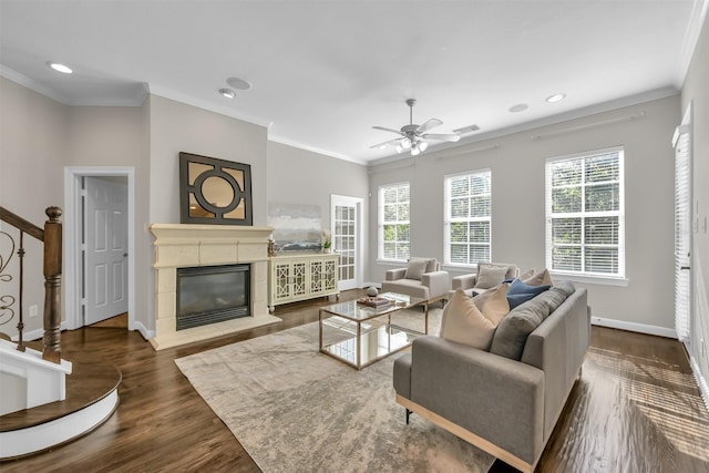living area with ornamental molding, a glass covered fireplace, baseboards, dark wood-type flooring, and a ceiling fan