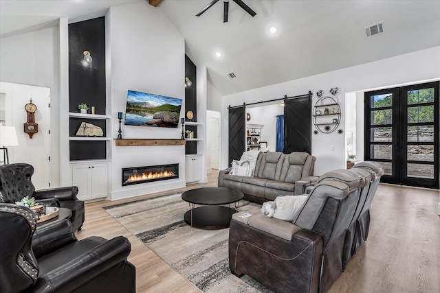 224 Kellog, Fischer, TX 78623 - living area featuring high vaulted ceiling, light wood-style flooring, a barn door, built in features, and a glass covered fireplace