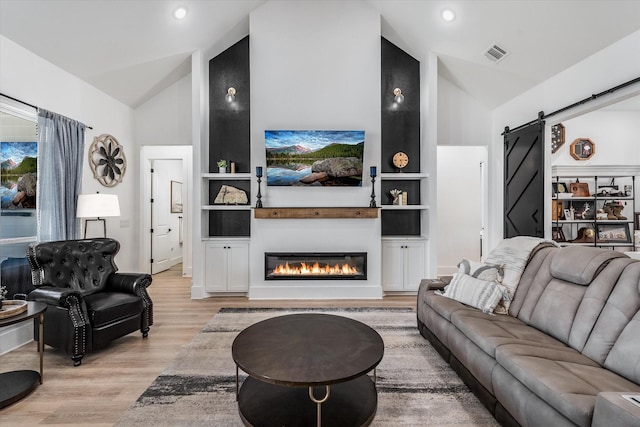 224 Kellog, Fischer, TX 78623 - living room with a barn door, light wood-type flooring, built in features, a glass covered fireplace, and high vaulted ceiling