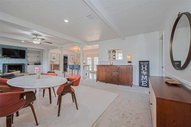 13018 Vernon Rd, Cypress, TX 77429 - dining room featuring a textured ceiling, beamed ceiling, a stone fireplace, a ceiling fan, and light carpet