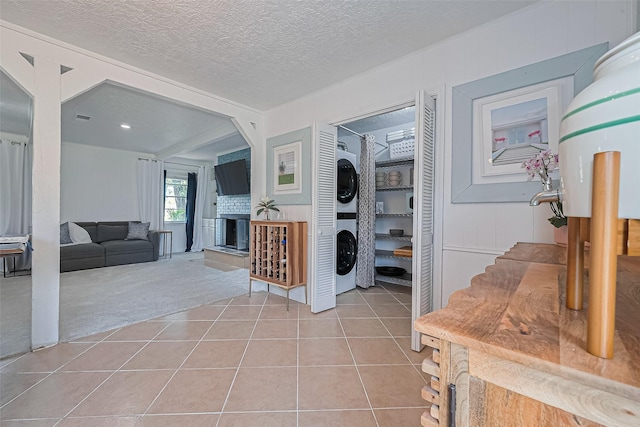 13018 Vernon Rd, Cypress, TX 77429 - entryway featuring stacked washer and clothes dryer, light tile patterned flooring, a fireplace with raised hearth, a textured ceiling, and light carpet
