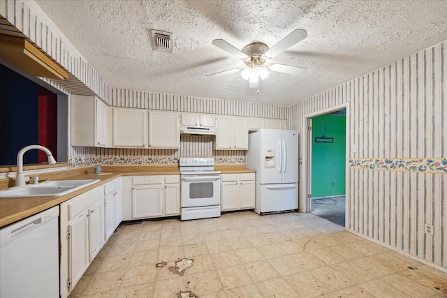 kitchen with white appliances, a sink, under cabinet range hood, light floors, and a textured ceiling