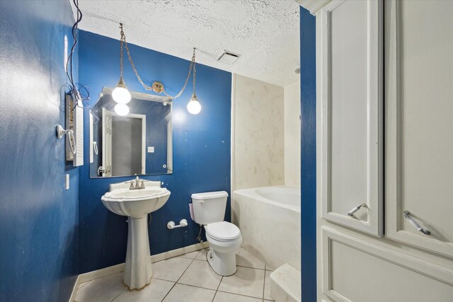 bathroom with tile patterned floors, a textured ceiling, toilet, a bathtub, and baseboards