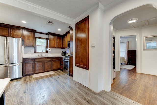708 Gresham St, Baytown, TX 77520 - kitchen with crown molding, appliances with stainless steel finishes, a sink, arched walkways, and light wood-style flooring