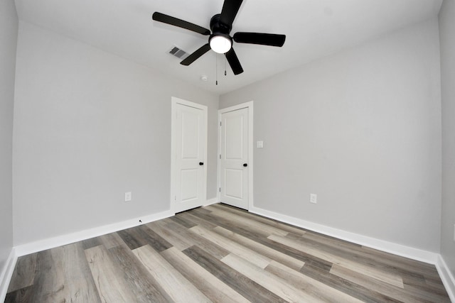 spare room with baseboards, a ceiling fan, wood finished floors, and visible vents