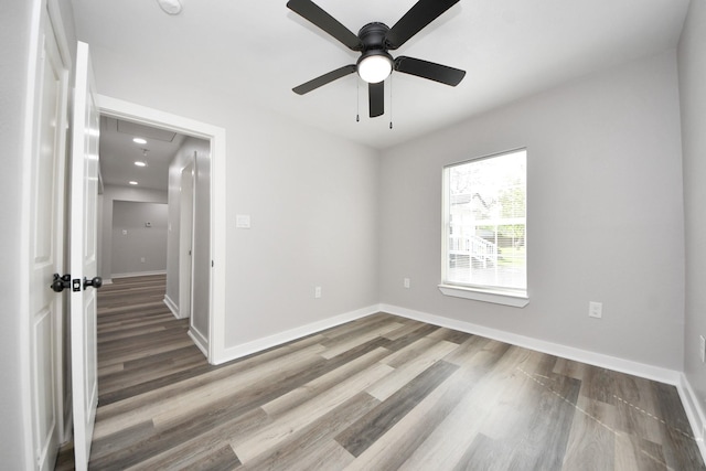 spare room featuring baseboards, a ceiling fan, attic access, and wood finished floors