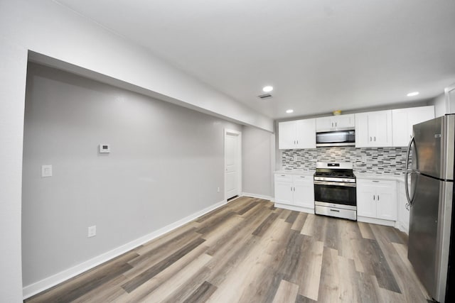 kitchen featuring decorative backsplash, white cabinetry, appliances with stainless steel finishes, and wood finished floors