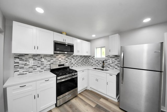kitchen featuring white cabinets, a sink, light countertops, light wood-style flooring, and stainless steel appliances