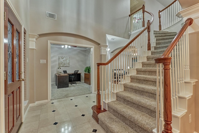 carpeted foyer featuring tile patterned floors, baseboards, stairs, arched walkways, and a high ceiling