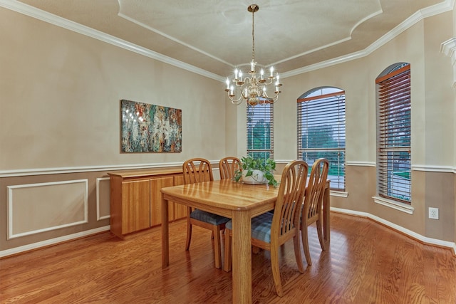 dining space featuring a chandelier, light wood finished floors, crown molding, and wainscoting