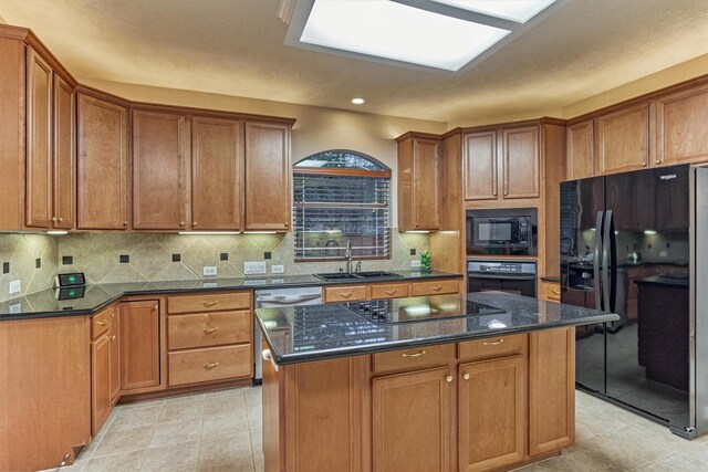 kitchen featuring black appliances, a sink, decorative backsplash, brown cabinets, and a center island