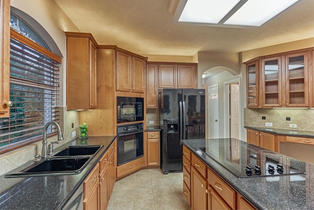 kitchen featuring black appliances, a sink, arched walkways, and brown cabinets