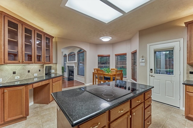 kitchen with black electric stovetop, tasteful backsplash, a kitchen island, brown cabinetry, and light tile patterned flooring