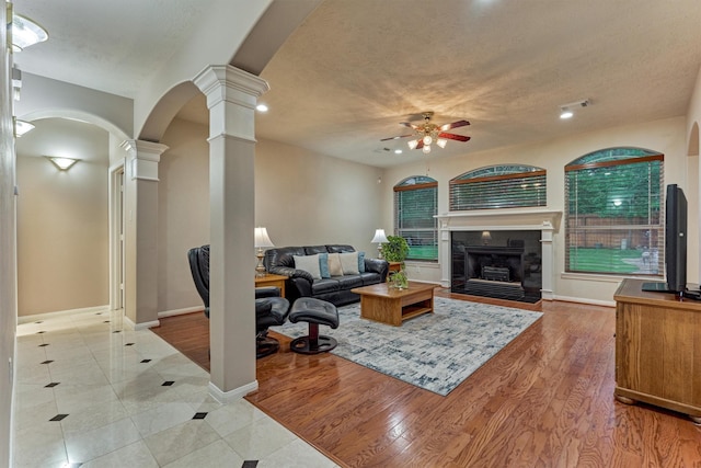 tiled living room with decorative columns, a ceiling fan, recessed lighting, a fireplace with flush hearth, and arched walkways