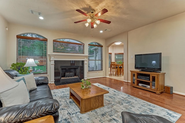 living area with a ceiling fan, arched walkways, healthy amount of natural light, wood finished floors, and recessed lighting