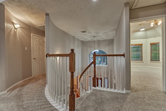 hall with an upstairs landing, carpet, a textured ceiling, and baseboards