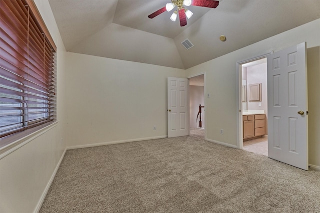 unfurnished bedroom featuring light colored carpet, vaulted ceiling, connected bathroom, baseboards, and ceiling fan