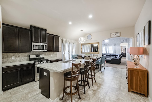 kitchen with a kitchen island with sink, tasteful backsplash, light countertops, lofted ceiling, and stainless steel appliances