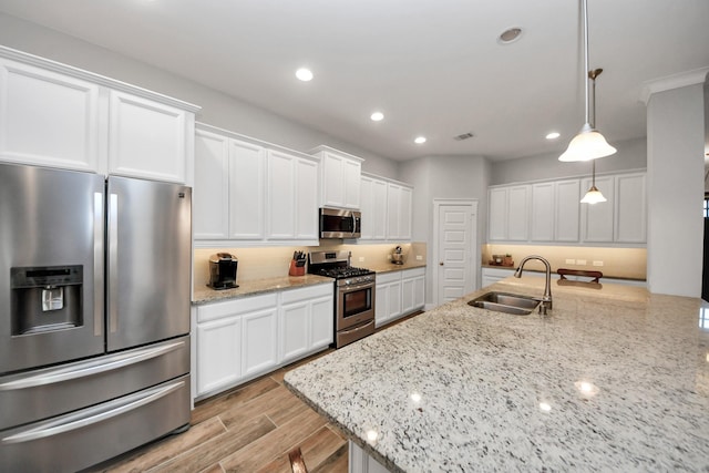 kitchen with appliances with stainless steel finishes, a sink, white cabinetry, decorative backsplash, and hanging light fixtures