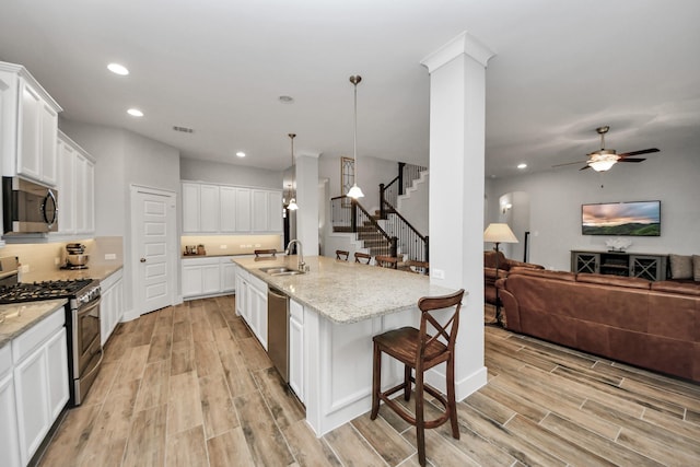 kitchen featuring appliances with stainless steel finishes, a sink, light wood finished floors, open floor plan, and recessed lighting